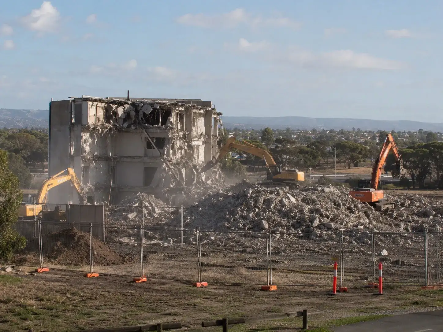 Two excavators demolishing a large structure with Adelaide skyline in background