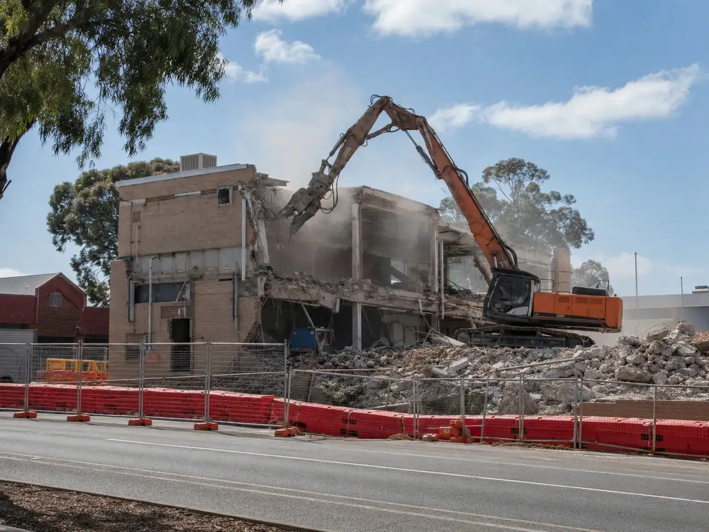 Large excavator demolishing a multi-storey building with dust and safety barriers