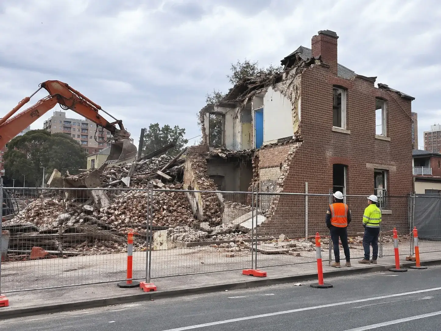 Site supervisors in hi-vis watching controlled house demolition in Adelaide