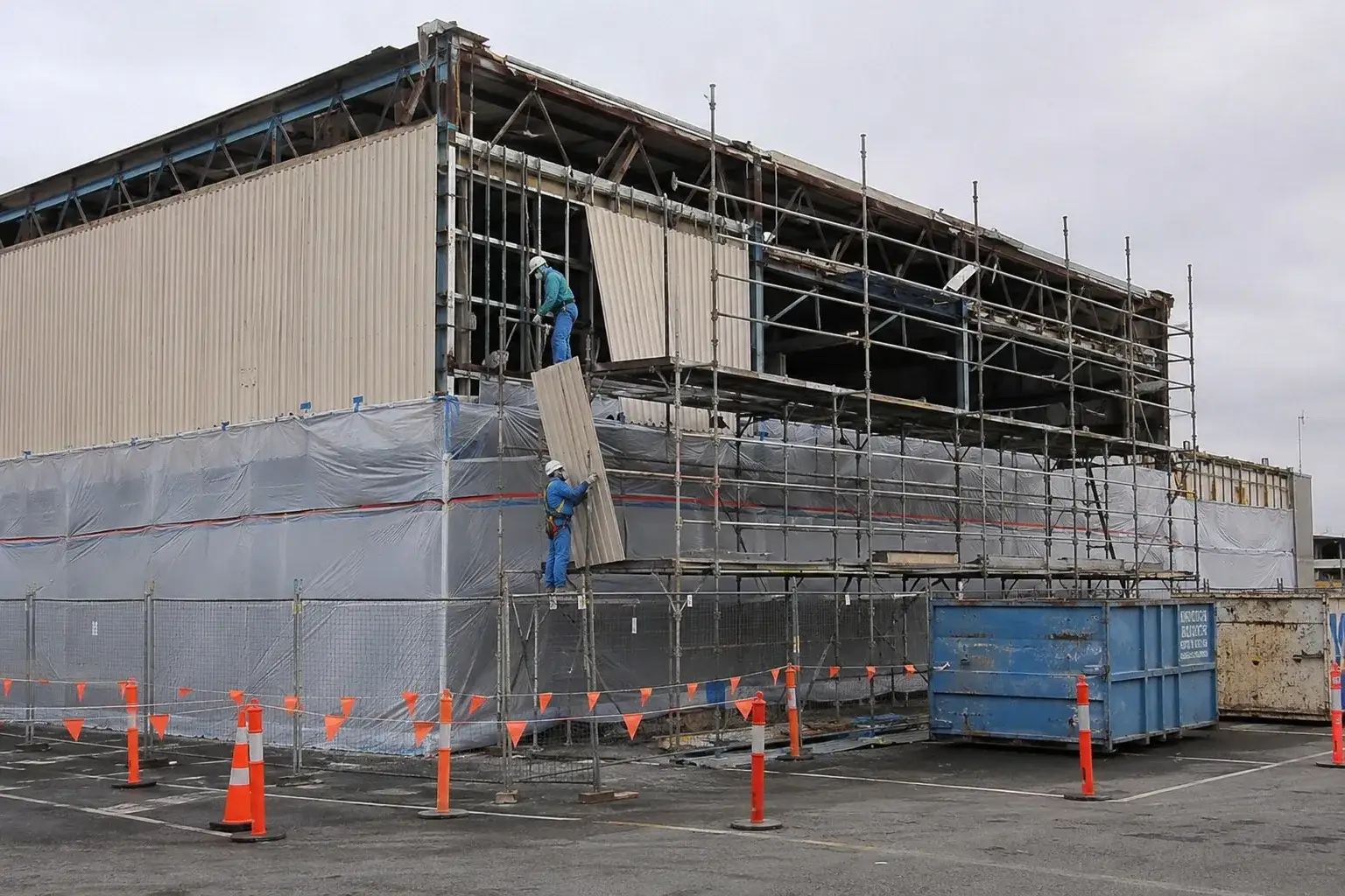 Workers in containment suits removing asbestos cladding from an industrial building on scaffolding